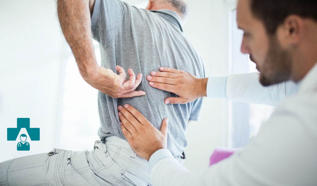 Closeup rear low angle view of an early 60's senior gentleman having some back pain. He's at doctor's office having medical examination by a male doctor. The patient is pointing to his lumbar region.